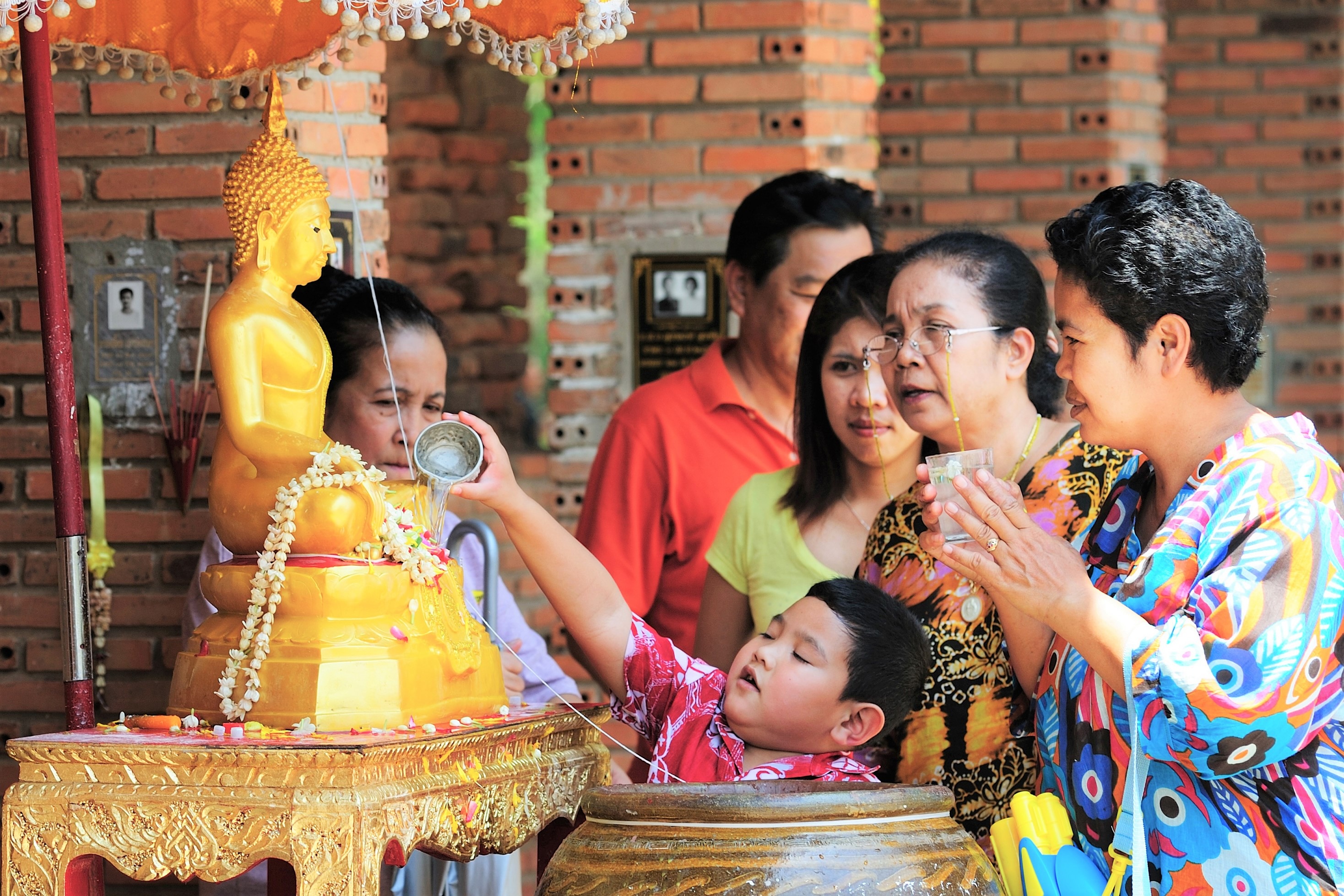 Family performing Song Nam Phra ritual with Buddha statue